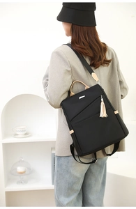 Rear view of model wearing a stylish black and white nylon backpack with tassel detail