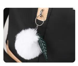 Dettaglio dello zaino nero in nylon con pompon bianco e ciondolo a foglia verde
