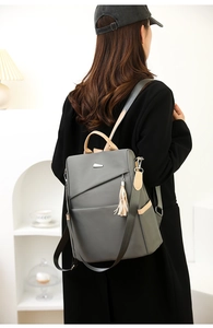 Detail of gray nylon backpack featuring brown straps and silver metal logo on model
