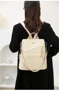 Detail of off-white nylon backpack showing metallic nameplate and leather tassel accessory