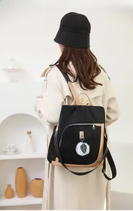 Vista posteriore dello zaino nero con profili beige e ciondolo di peluche su un modello