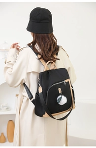 Dettaglio dello zaino in nylon nero con finiture in pelle beige e ciondolo a pompon