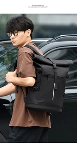 Outdoor side view of a black roll-top backpack featuring a vertical reflective safety strip