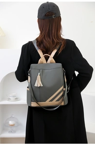 Detail of grey PU leather backpack with contrast trim, side stripes, and tassel charm