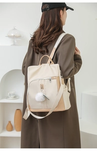 Dettaglio di uno zaino in nylon beige e kaki con ciondolo a pompon su una modella