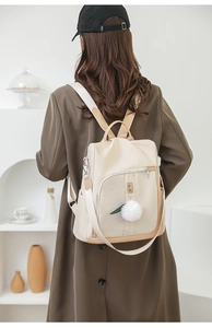 Dettaglio zaino beige elegante con bordi marroni e ciondolo a pompon sulla schiena