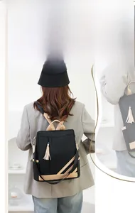 Detail of black PU leather backpack showing contrasting beige straps and tassel pendant