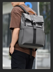 Detail of grey roll-top waterproof backpack featuring metal buckle and orange handle