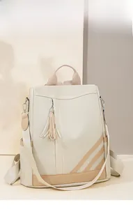 Detail view of cream-colored backpack with brown diagonal stripes and fringe charm