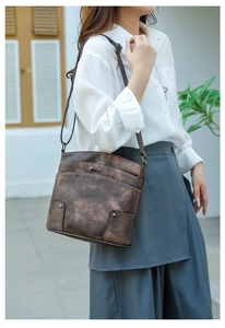 Detail of vintage dark brown PU leather crossbody bag with metallic logo and studs