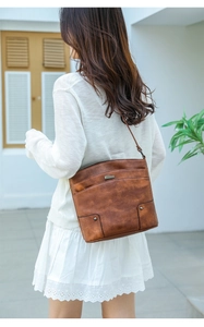 Detail of vintage brown PU leather handbag texture with metal plaque on white knit outfit