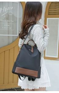 Sac à dos en nylon noir et cuir marron porté par un mannequin dans un décor de rue chic