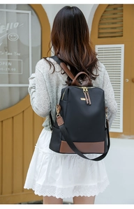 Détail d'un sac à dos en nylon noir avec bordures en similicuir marron porté par un modèle