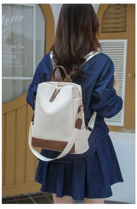 Détail d'un sac à dos en nylon crème avec finitions en cuir marron porté par un mannequin