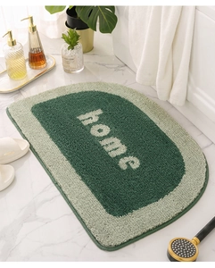 Detail of a semi-circular green bath mat with home text on a marble floor setting