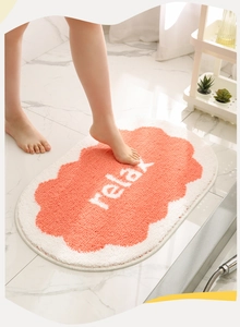 Detail of plush orange and white oval bath mat with relax text on marble floor