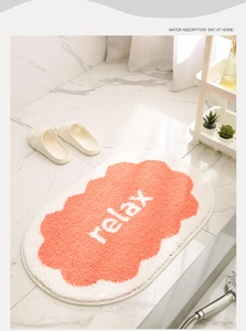 Detail of orange and white oval bath mat with relax text on marble floor
