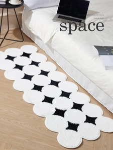 Close-up of fluffy wave-edged bedside rug with black diamond patterns on light wood floor