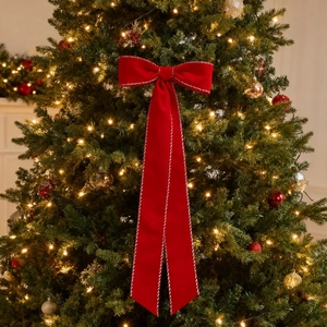 Red flocked velvet Christmas bow with white stitched edges hanging on a lighted tree