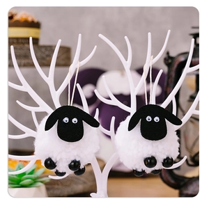 Close-up of cute black and white sheep plush ornaments hanging on a white branch
