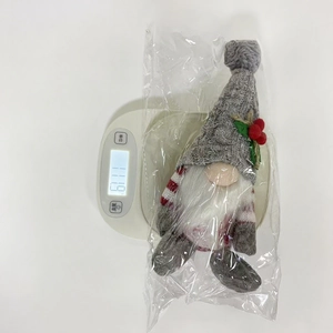 Weihnachtswichtel mit grauer Strickmütze und Stechpalmenbeere wiegt 111,9g auf digitaler Waage