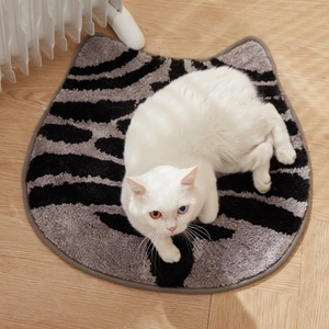 Zebra striped cat-shaped plush bath mat on wooden floor with a white cat sitting nearby