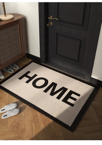 Detailed top view of beige HOME doormat with black border on herringbone wood flooring