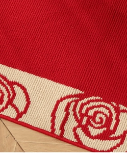 Detail of red festive door mat showing textured rose pattern on herringbone wood floor