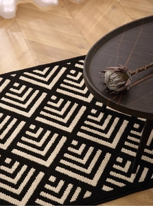 Close-up of black and white geometric pattern indoor doormat on light wooden floor