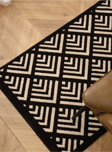 Detail of black and white geometric pattern doormat on light wood floor with a chair
