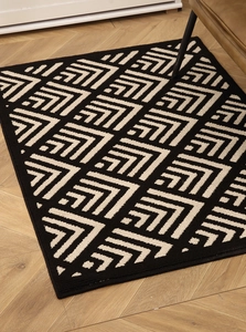 Detailed close-up of modern geometric plaid door mat on light herringbone wood floor