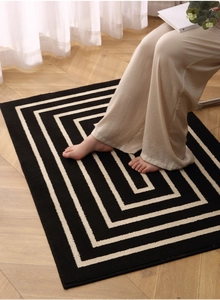 Detail of high-end black and white geometric spiral rug on light herringbone wood floor