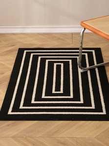 Detail view of black and white geometric rectangle rug on wooden floor with chair