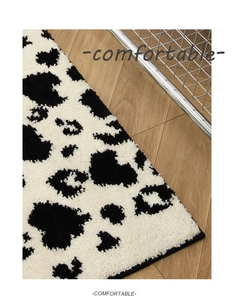 Close-up of fluffy black and white cow print plush rug texture on wooden floor