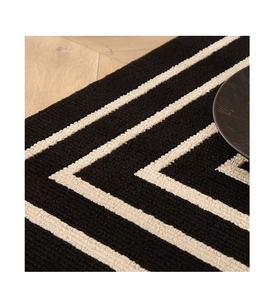Detail of geometric black and white textured doormat on a warm wooden floor