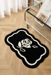 Detalle de alfombra de baño de rosa con bordes ondulados en blanco y negro sobre madera