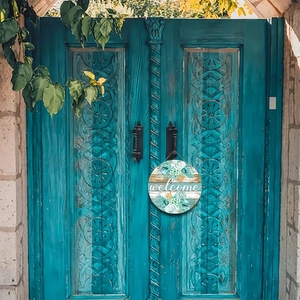 Round wooden welcome sign with succulents hanging on vintage blue double doors