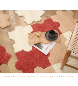 Macro detail of modular puzzle plush rug pieces in ivory and brick red on wood floor