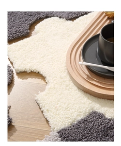 Detail of plush grey and beige puzzle carpet texture on a warm wooden floor