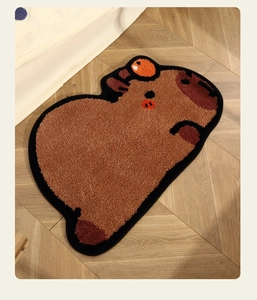 Close-up of soft tufted capybara bath mat with orange detail on light wood floor
