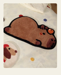 Detailed close-up of a brown capybara plush tufted bath mat on a soft bed