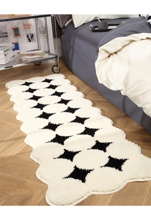 Detail of plush cream runner rug with black star patterns and unique wavy scalloped edges