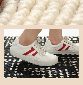 Λεπτομέρεια από λευκά δερμάτινα sneakers με κόκκινες ρίγες σε καρό χαλί