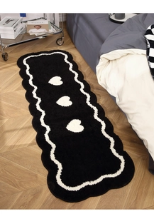 Detailed view of black wavy bedside rug with white hearts on herringbone wood floor
