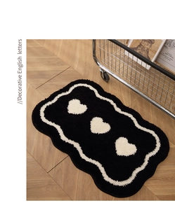 Detail of soft black plush bedside rug with three white hearts and wavy borders