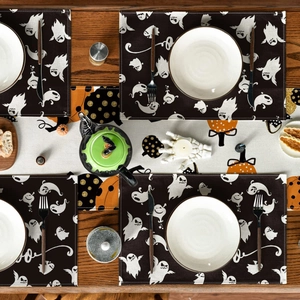 Halloween table runner and ghost placemats set displayed on a dark wooden dining table