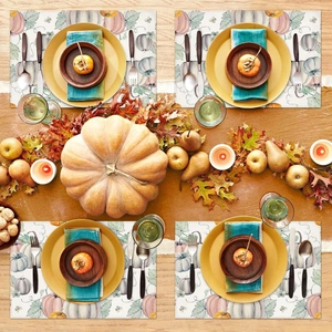Detail of four fall placemats with pumpkin and maple leaf prints on a wooden table