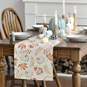 Detail of autumn table runner with pumpkin and maple leaf print on wood surface