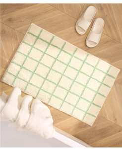 Detail of soft tufted bath mat with green grid pattern on light wood floor with slippers