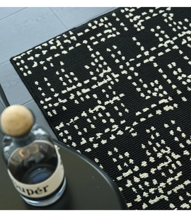 Detail of modern black woven rug with cream geometric pattern on grey wooden floor